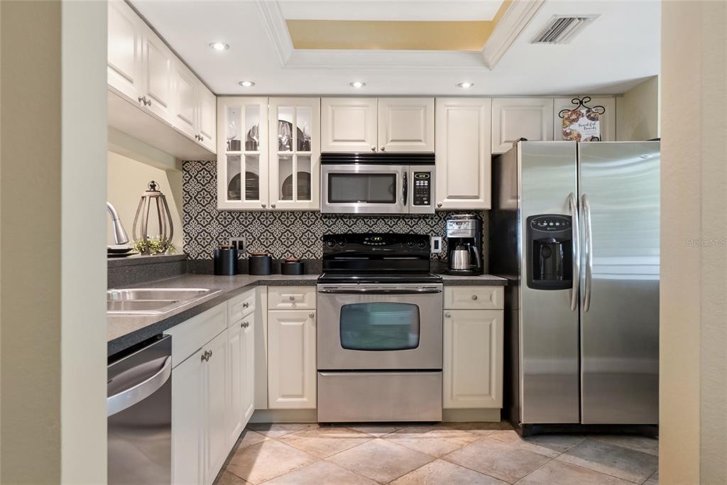 A kitchen features white cabinets, stainless steel appliances, a patterned backsplash, and tile flooring — 4242 MADEIRA COURT UNIT 3315, SARASOTA, FL