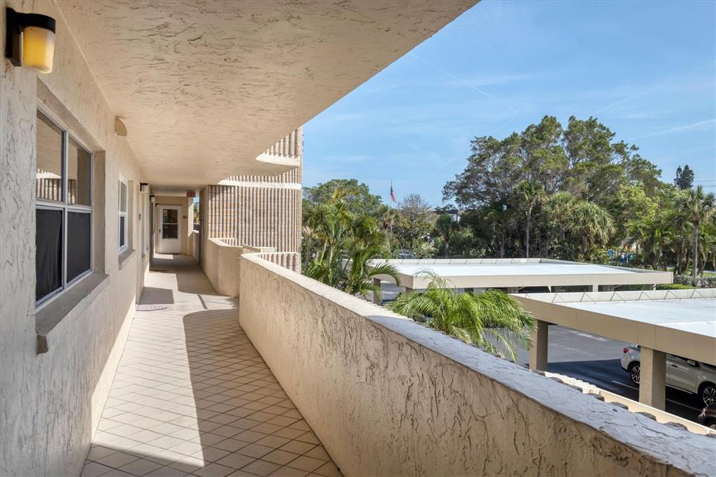 An outdoor apartment walkway with a tiled floor, stucco walls, and a view of parking — 4325 GULF OF MEXICO DRIVE UNIT 208, LONGBOAT KEY, FL