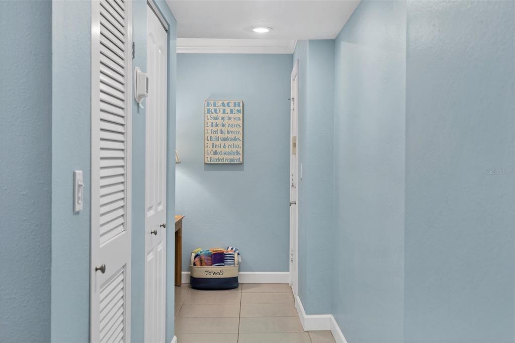 A hallway with light blue walls, tile flooring, louvered closet doors, and a decorative beach sign — 4325 GULF OF MEXICO DRIVE UNIT 208, LONGBOAT KEY, FL