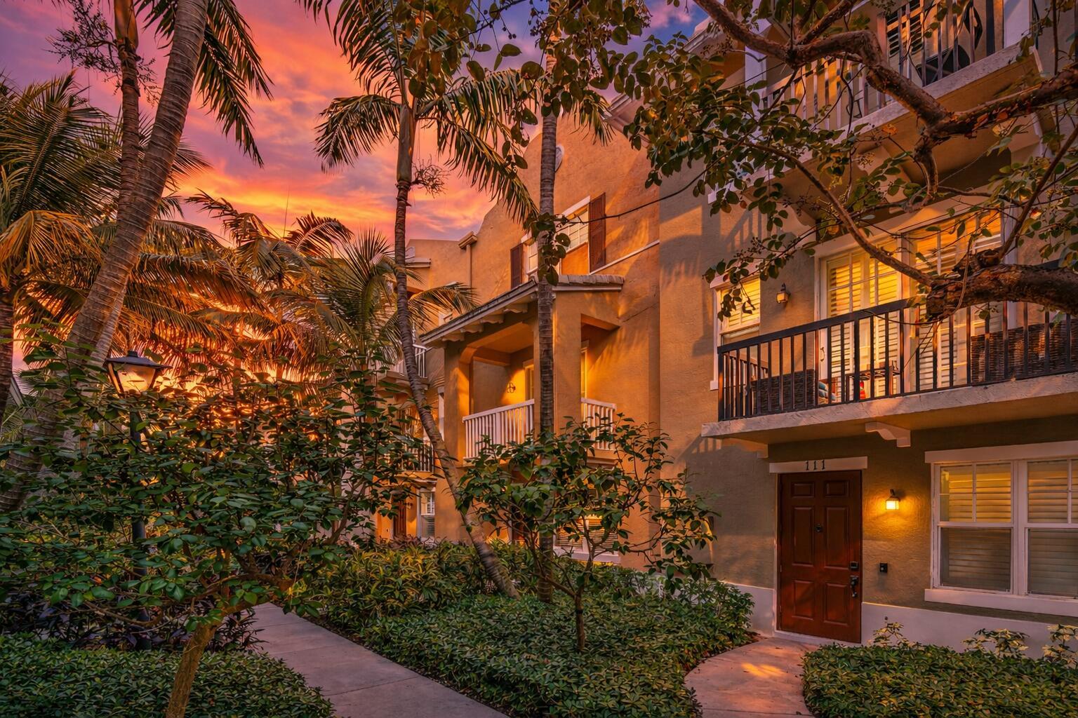 An exterior view of a multi-story apartment building with balconies, palm trees, and sunset lighting — 109 E Coda Circle, Delray Beach FL 33444, DELRAY BEACH, FL