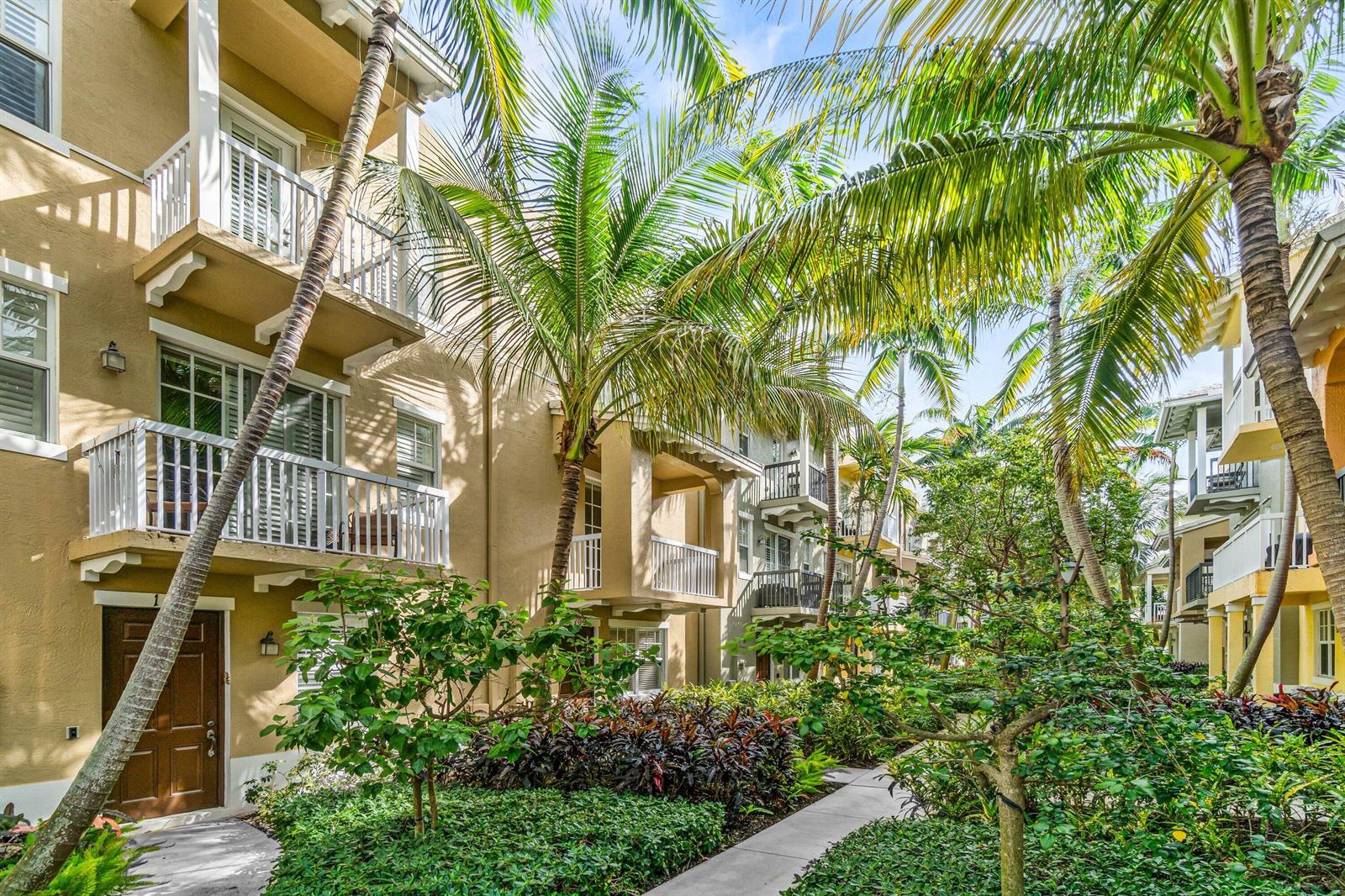 Exterior view of a multi-story apartment building with balconies and lush tropical landscaping — 109 E Coda Circle, Delray Beach FL 33444, DELRAY BEACH, FL