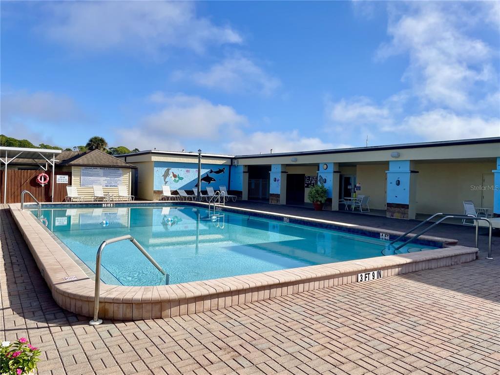 An outdoor swimming pool with a brick deck and a surrounding building under a blue sky — 6452 FLEETWOOD COURT, NORTH PORT, FL