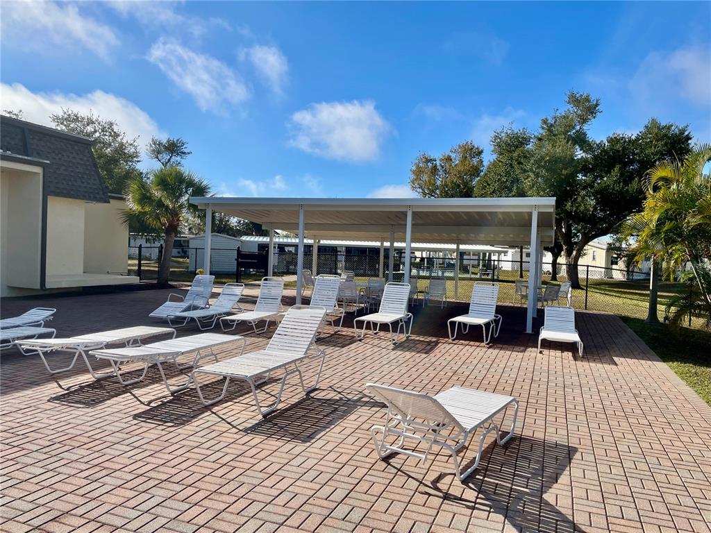 A paved pool deck features numerous white lounge chairs under a large metal patio cover — 6452 FLEETWOOD COURT, NORTH PORT, FL