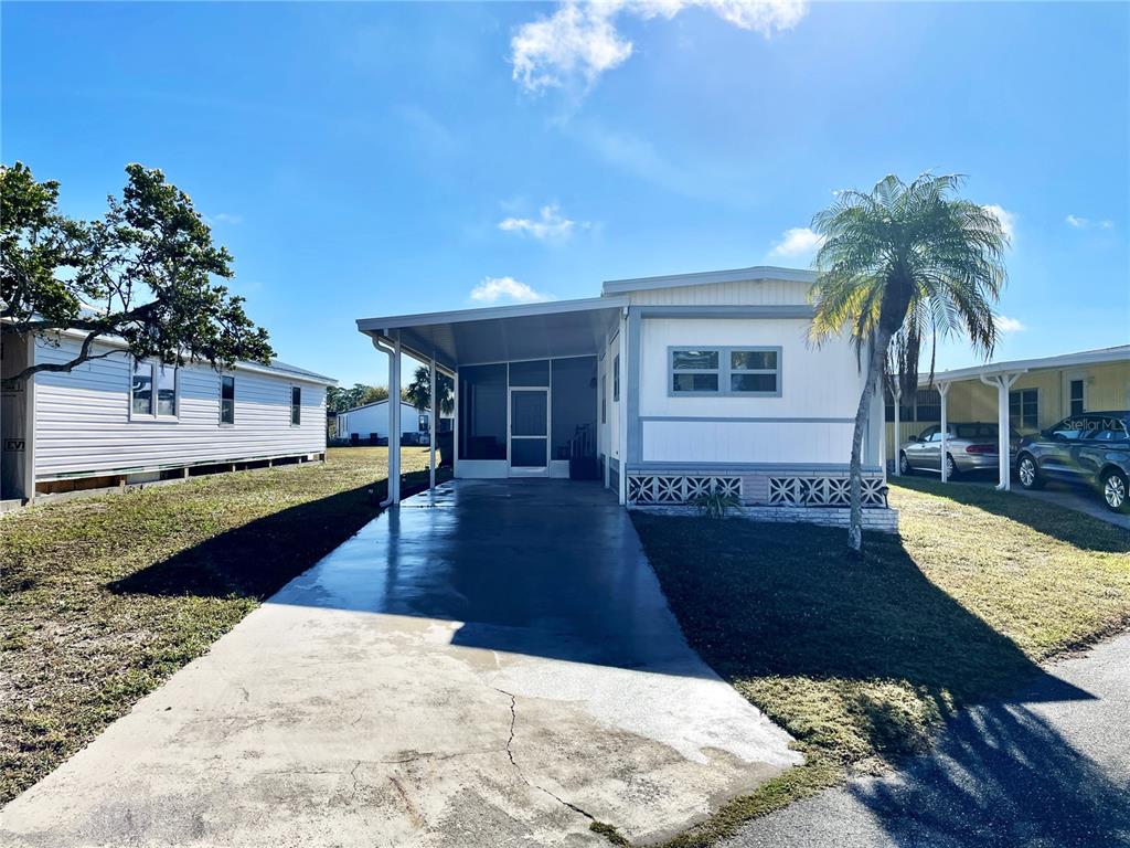 A single-story mobile home features a concrete driveway, a screened-in porch, and a palm tree — 6452 FLEETWOOD COURT, NORTH PORT, FL