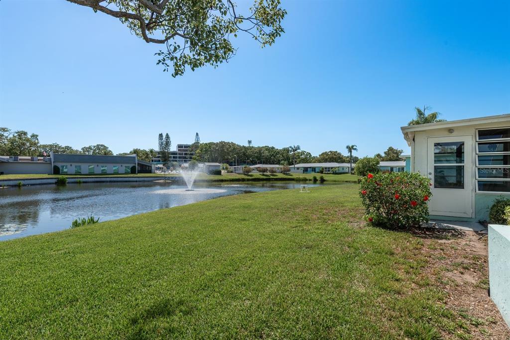 A grassy yard overlooks a pond with a fountain and surrounding residential buildings — 2738 SHERBROOKE LANE UNIT C, PALM HARBOR, FL