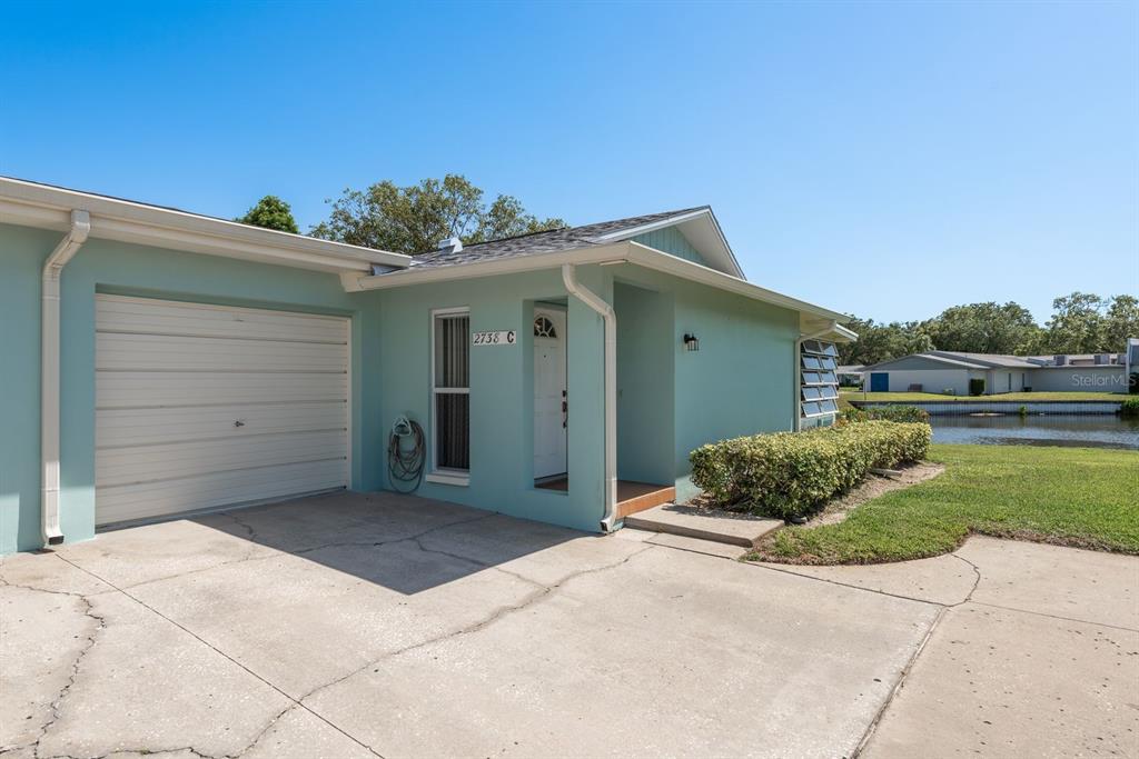 A light green exterior of a single-story home with a garage and a small lawn — 2738 SHERBROOKE LANE UNIT C, PALM HARBOR, FL