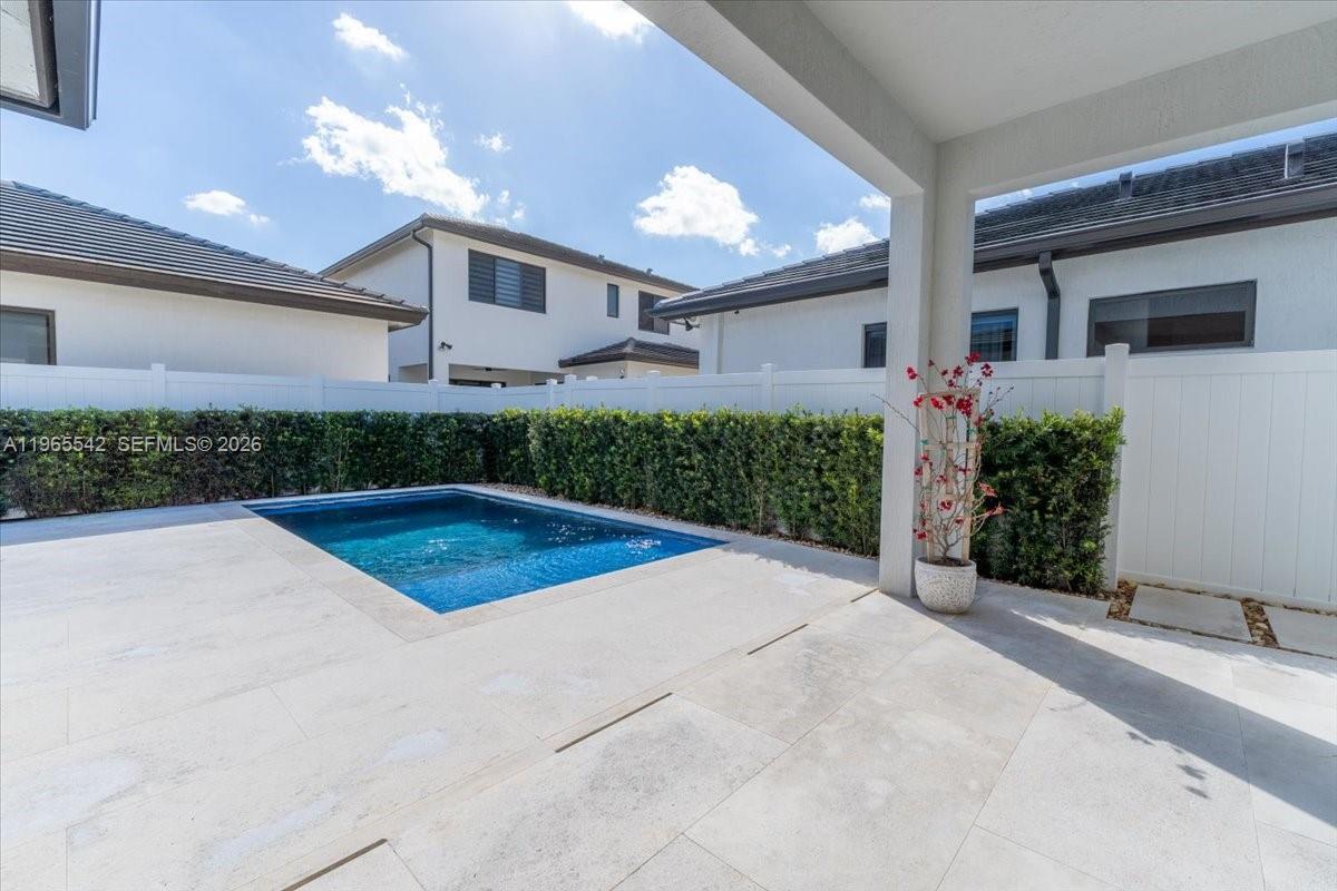 A backyard features a rectangular swimming pool, a paved patio, and a white privacy fence — 8096 NW 48th Ter, Doral FL 33166, DORAL, FL