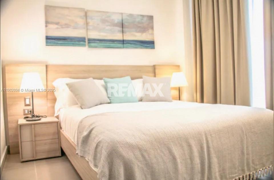A bedroom features a light wood headboard, matching nightstand, and three coastal-themed wall art panels — El cortesito Punta Cana # 1, PU, PU