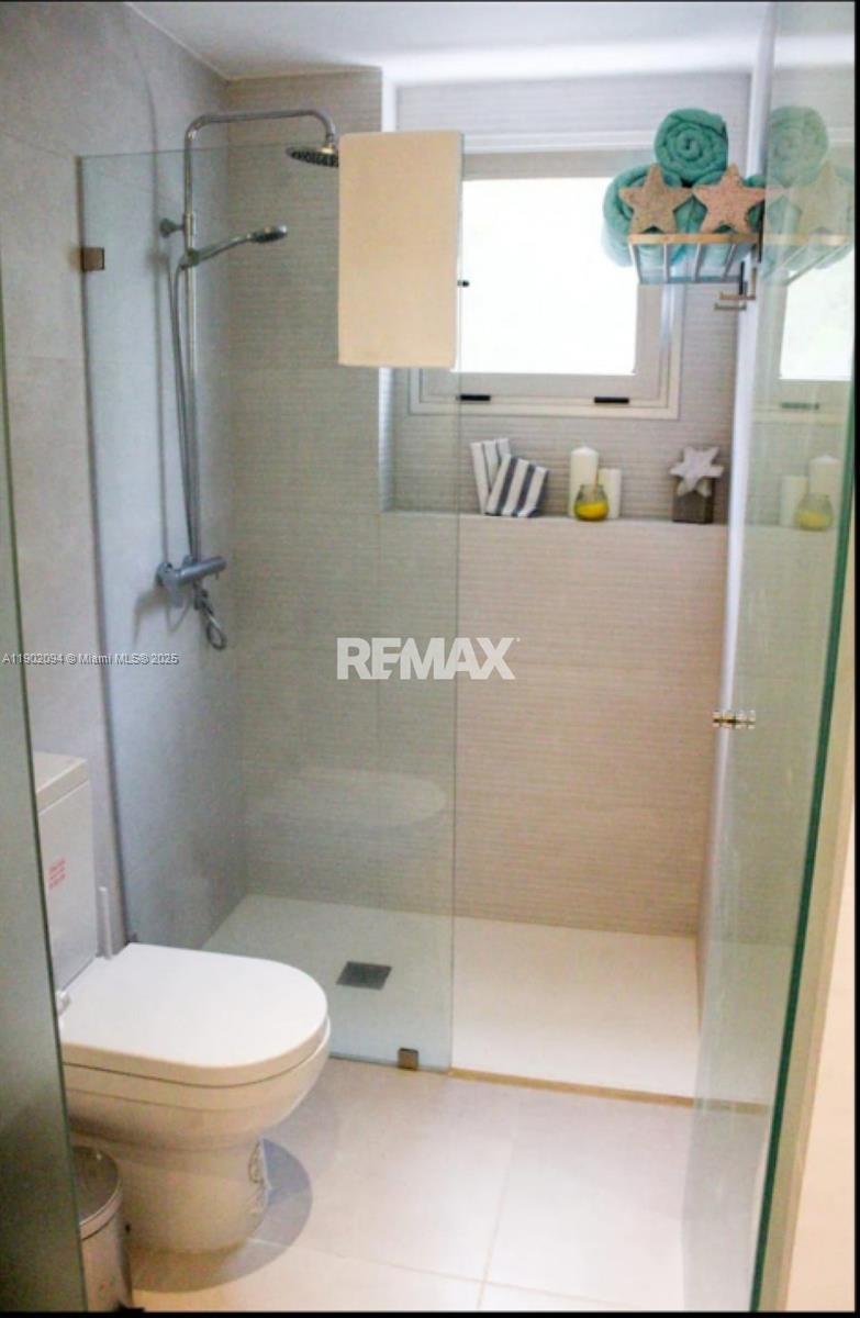 A modern bathroom features a glass-enclosed walk-in shower, a white toilet, and light-colored tile walls — El cortesito Punta Cana # 1, PU, PU