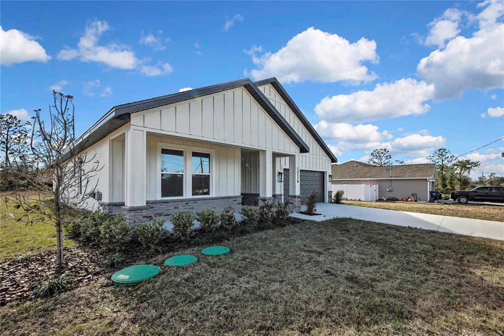 A single-story house with white vertical siding, a stone base, and a two-car garage — 13126 MEADOW SWALLOW AVENUE, BROOKSVILLE, FL