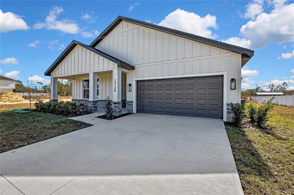 A single-story house with white board-and-batten siding, a stone base, and a two-car garage — 13126 MEADOW SWALLOW AVENUE, BROOKSVILLE, FL