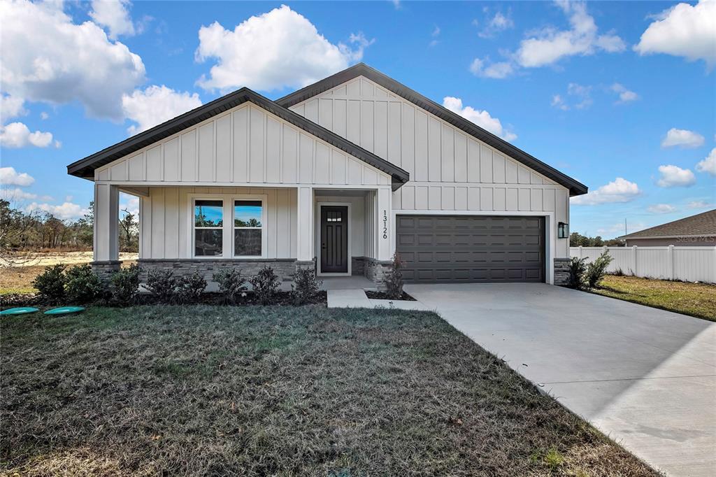 A single-story house features white vertical siding, stone accents, and a two-car garage — 13126 MEADOW SWALLOW AVENUE, BROOKSVILLE, FL