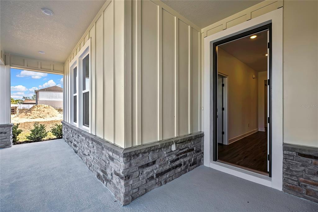 A covered porch features board-and-batten siding, stone veneer, and an open doorway leading inside — 13126 MEADOW SWALLOW AVENUE, BROOKSVILLE, FL