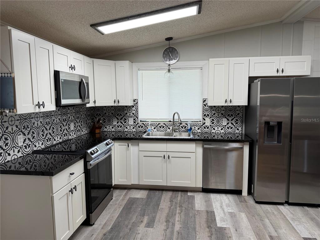 A kitchen features white cabinets, black countertops, patterned tile backsplash, and stainless steel appliances — 3107 IDA DRIVE, ELLENTON, FL