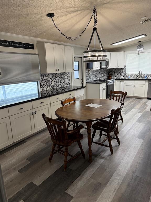 A kitchen with white cabinets, black countertops, patterned backsplash, and a wooden dining table — 3107 IDA DRIVE, ELLENTON, FL