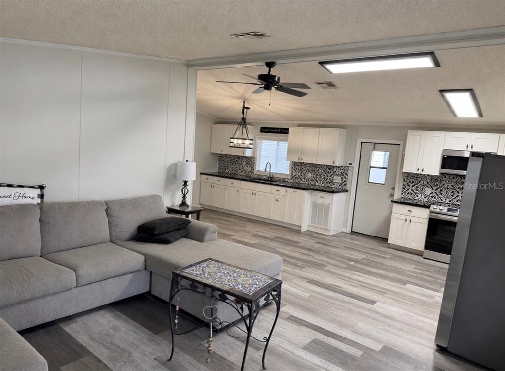 A living room with a gray sectional sofa opens into a kitchen with white cabinets — 3107 IDA DRIVE, ELLENTON, FL