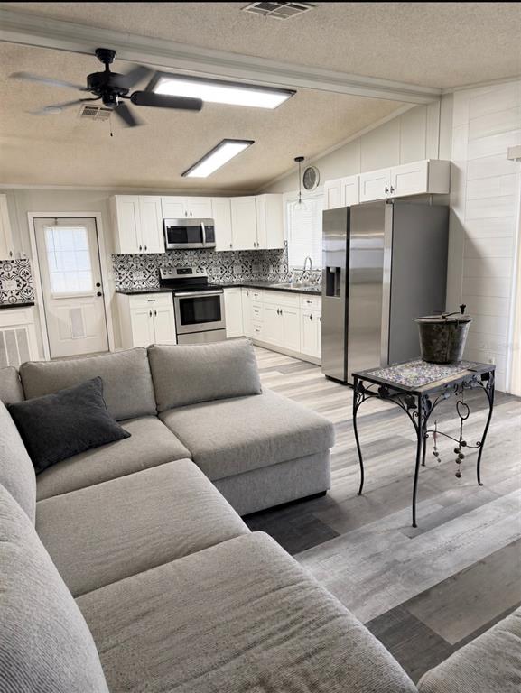 A kitchen with white cabinets and patterned backsplash opens to a living area with sectional — 3107 IDA DRIVE, ELLENTON, FL
