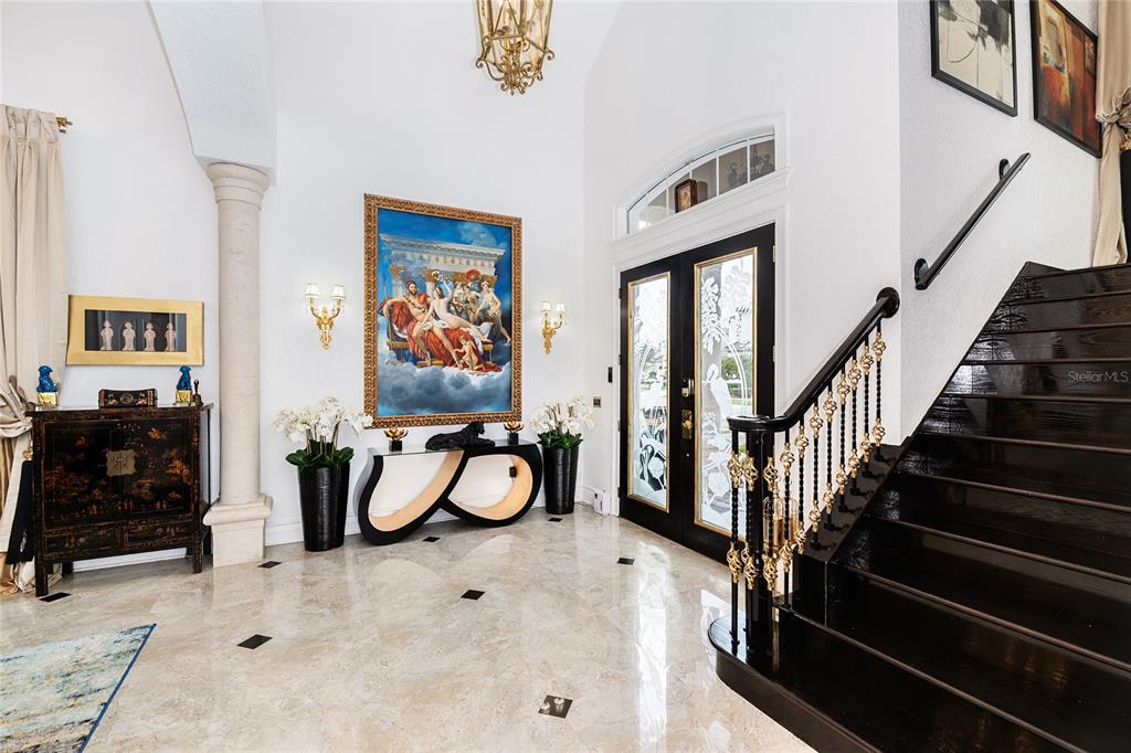 A grand foyer features a dark wood staircase, marble flooring, and a large classical painting — 7409 GATHERING COURT, REUNION, FL