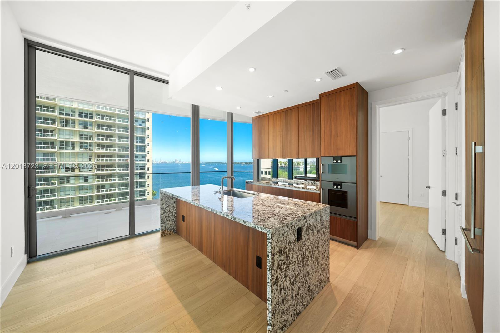 A modern kitchen features a granite island, wood cabinetry, and floor-to-ceiling windows overlooking the water — 175 SE 25 RD # 804, Miami FL 33129, MIAMI, FL