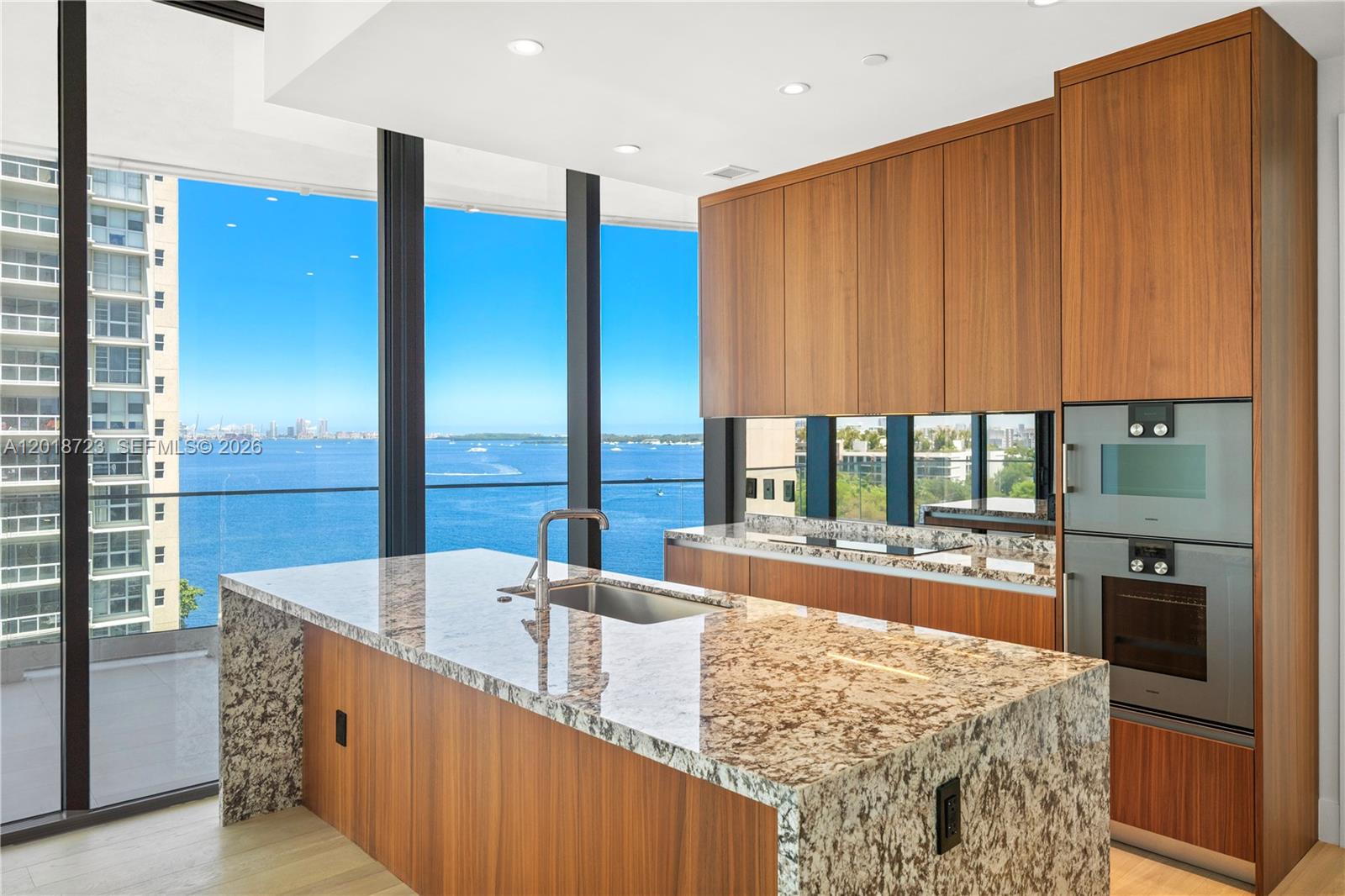 A modern kitchen features wood cabinetry, granite countertops, and floor-to-ceiling windows overlooking the ocean — 175 SE 25 RD # 804, Miami FL 33129, MIAMI, FL