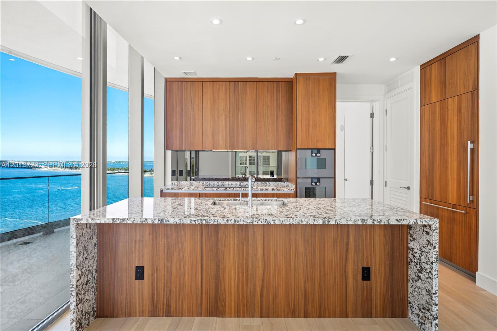 A modern kitchen features wood cabinetry, granite countertops, a large island, and floor-to-ceiling windows — 175 SE 25 RD # 804, Miami FL 33129, MIAMI, FL