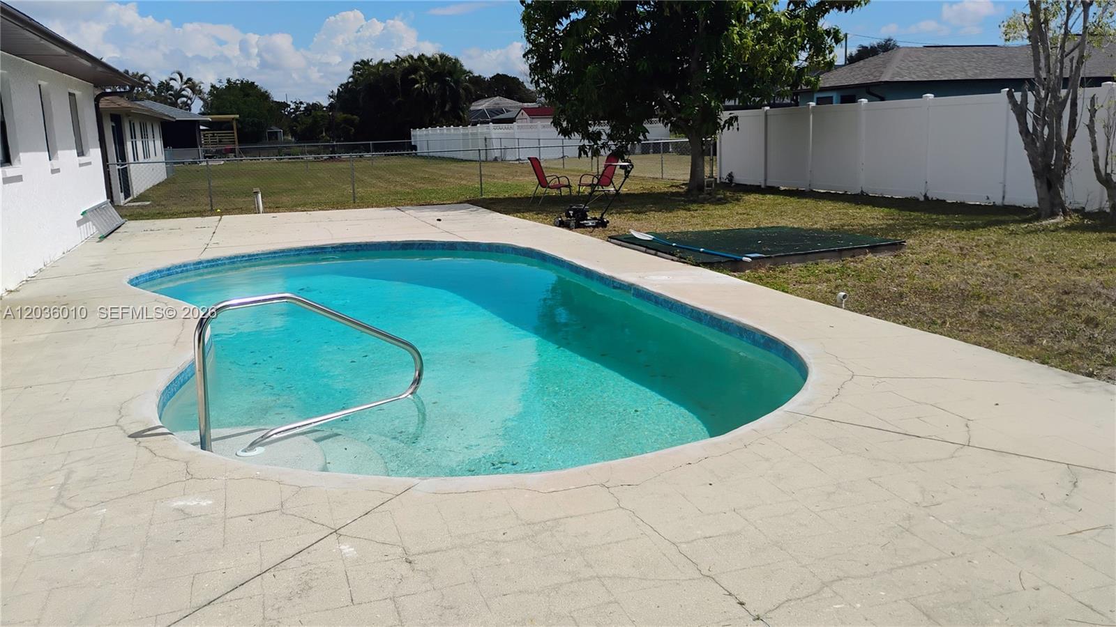 A backyard features a swimming pool with a metal handrail and a white privacy fence — 1404 SE 19TH St., Cape Coral FL 33990, CAPE CORAL, FL