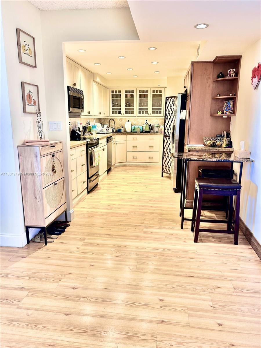 A kitchen features light wood flooring, white cabinetry, and a small dark wood breakfast bar — 600 Three Islands Blvd # 905, Hallandale Beach FL 33009, HALLANDALE BEACH, FL