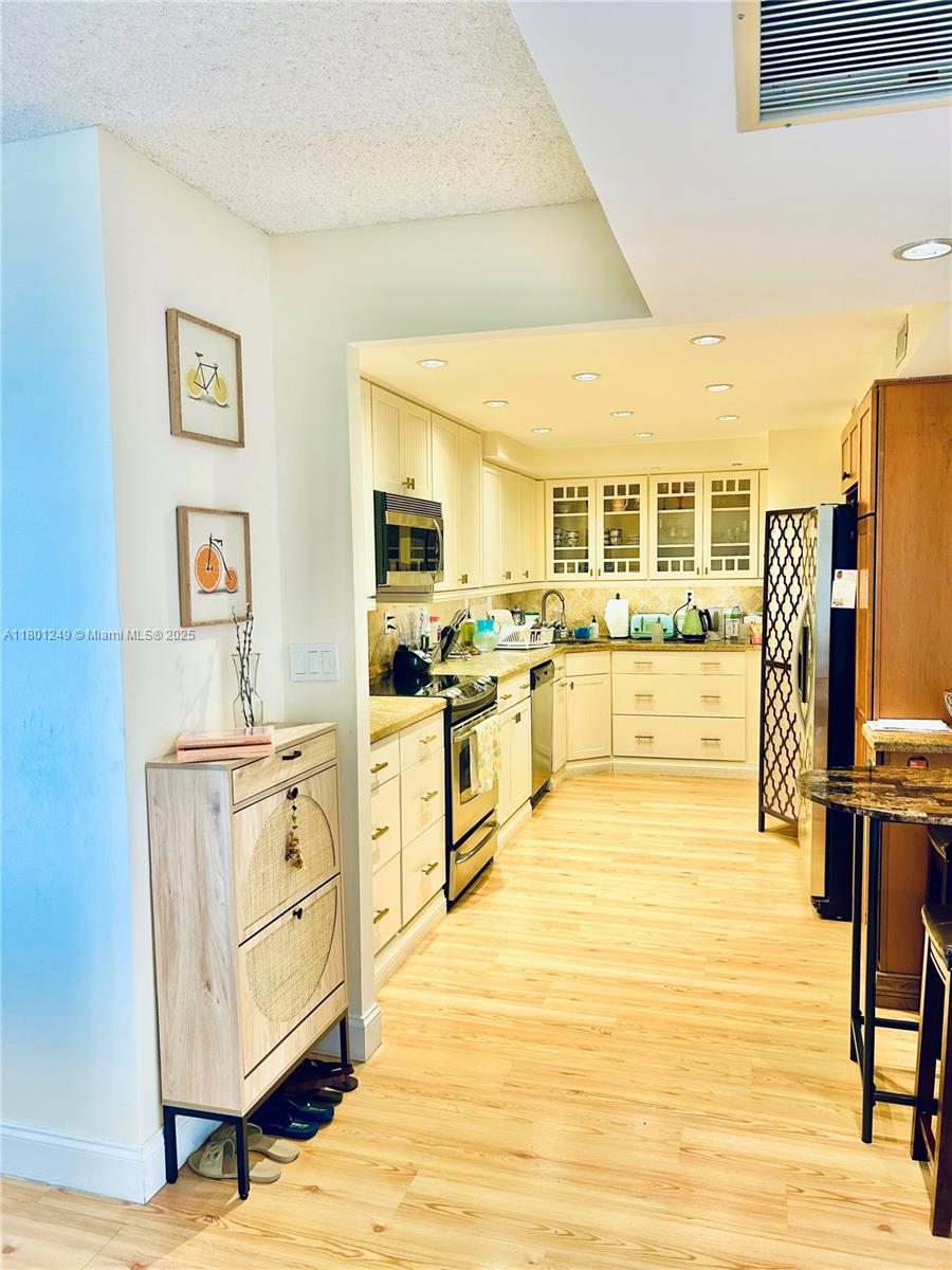 A kitchen features light-colored cabinetry, stainless steel appliances, and wood-look flooring — 600 Three Islands Blvd # 905, Hallandale Beach FL 33009, HALLANDALE BEACH, FL