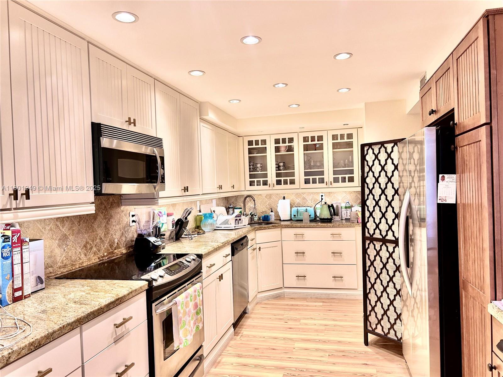 A kitchen features light-colored cabinets, granite countertops, stainless steel appliances, and a decorative room divider — 600 Three Islands Blvd # 905, Hallandale Beach FL 33009, HALLANDALE BEACH, FL