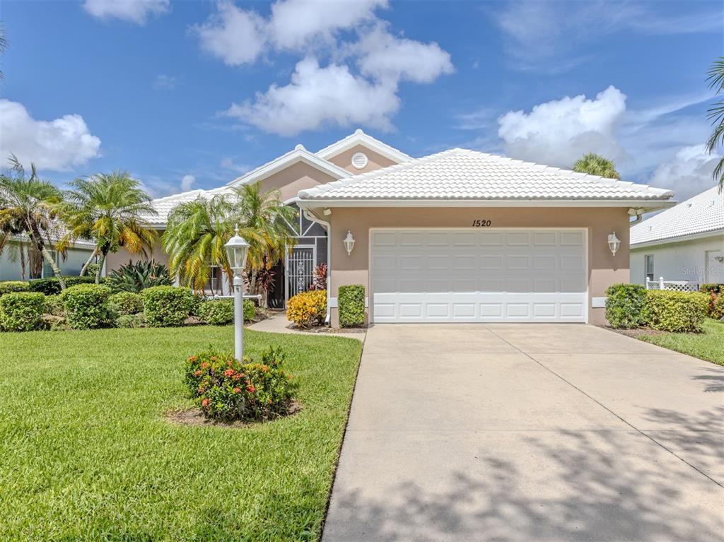 A single-story house with a white tile roof, beige stucco walls, and a two-car garage — 1520 JASPER COURT, VENICE, FL