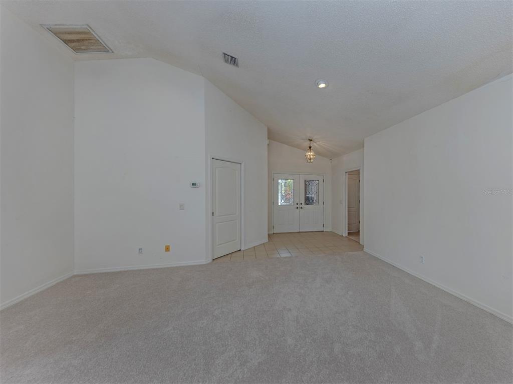 A spacious room with white walls, beige carpeting, a vaulted ceiling, and a tiled entryway — 1520 JASPER COURT, VENICE, FL