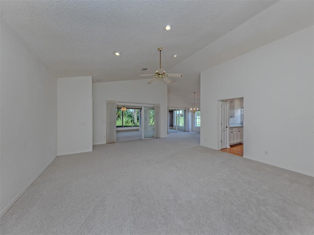 A spacious, carpeted living room features vaulted ceilings, a ceiling fan, and sliding glass doors — 1520 JASPER COURT, VENICE, FL