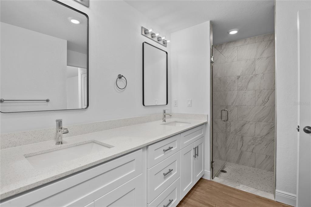 A modern bathroom features a double vanity with white cabinets, quartz countertops, and a walk-in shower — 2286 ATWATER DRIVE, NORTH PORT, FL
