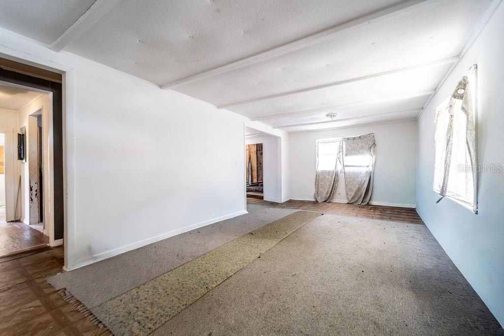 An empty room features white walls, a beamed ceiling, and a worn carpet runner — 2900 STATE ROAD 11, DELAND, FL