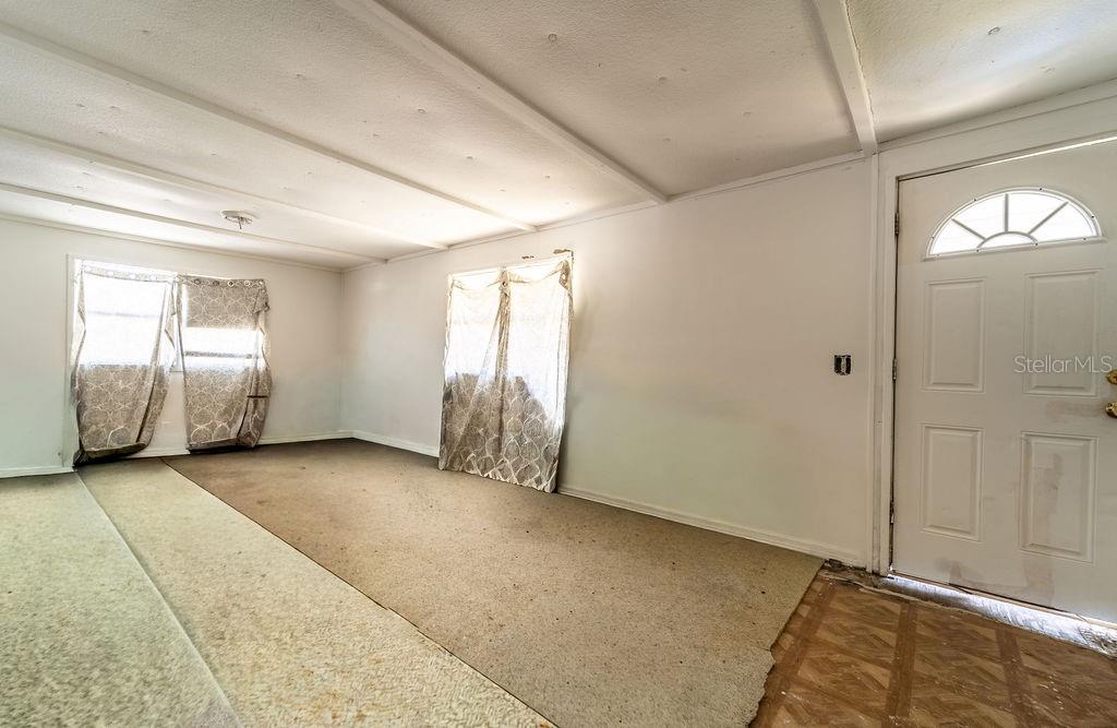 An empty room with white walls, carpeted flooring, two windows with curtains, and a door — 2900 STATE ROAD 11, DELAND, FL
