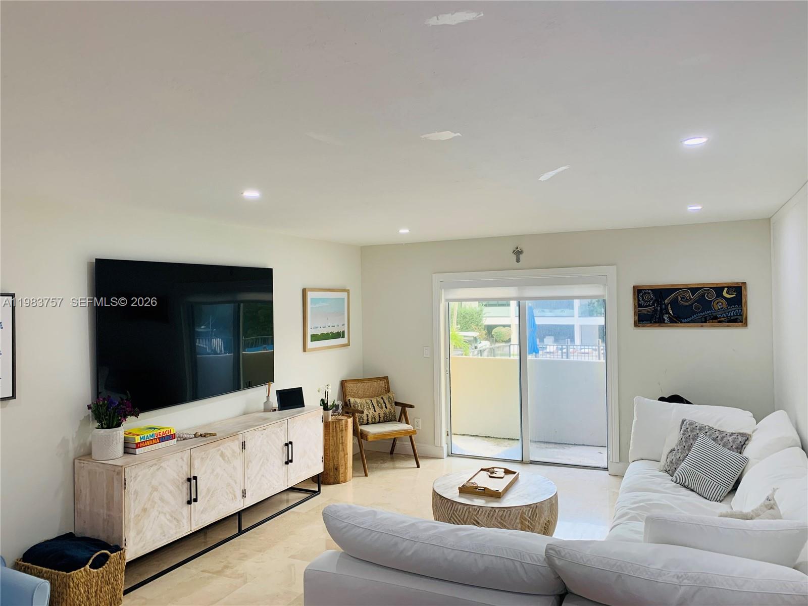 A living room features a large television, a white media console, and a sectional sofa — 6815 Edgewater Dr # 105, Coral Gables FL 33133, CORAL GABLES, FL