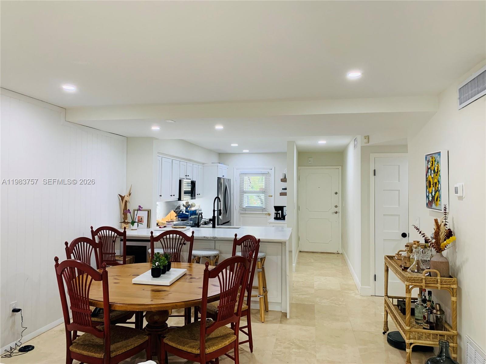A dining area with a wooden table and chairs sits adjacent to a white kitchen — 6815 Edgewater Dr # 105, Coral Gables FL 33133, CORAL GABLES, FL
