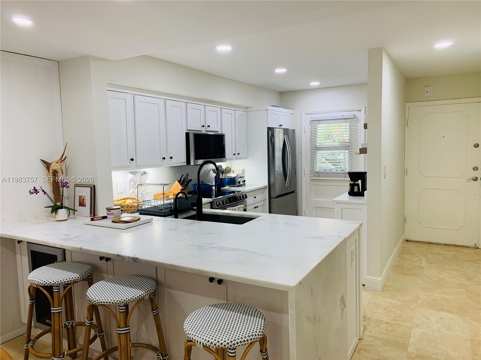 A kitchen features white cabinets, a marble-topped island with stools, and stainless steel appliances — 6815 Edgewater Dr # 105, Coral Gables FL 33133, CORAL GABLES, FL