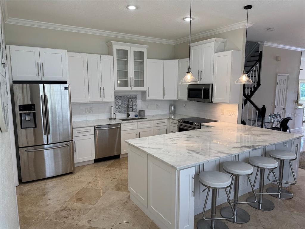 A kitchen features white cabinetry, a marble-topped island with stools, and stainless steel appliances — 1806 LAGO VISTA BOULEVARD, PALM HARBOR, FL