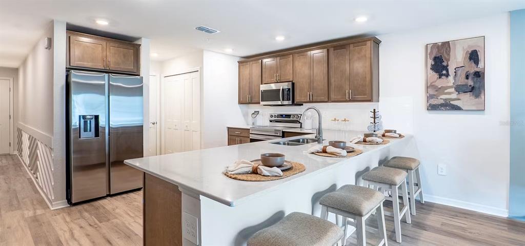 A modern kitchen features wood cabinets, stainless steel appliances, and a large white quartz island — 406 CHESAPEAKE DRIVE, ST CLOUD, FL