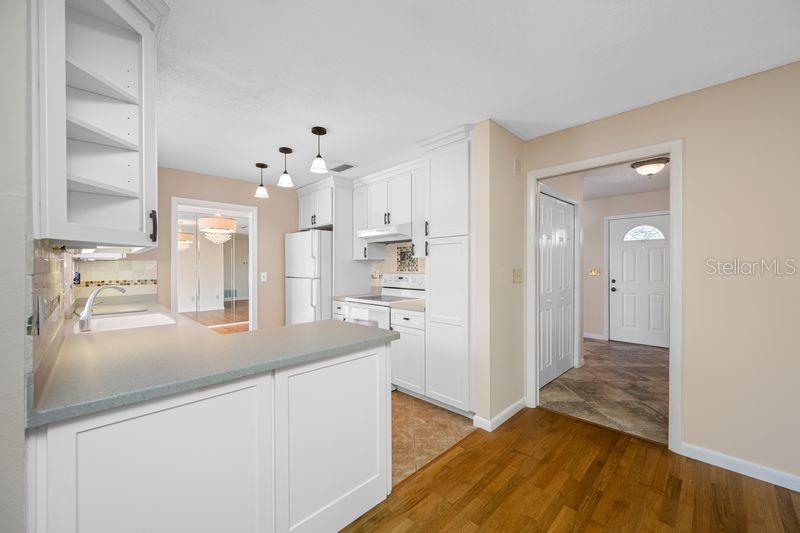 A kitchen with white cabinets, a gray countertop, and wood flooring, opening to a hallway — 3241 BUCKHORN DR, CLEARWATER, FL
