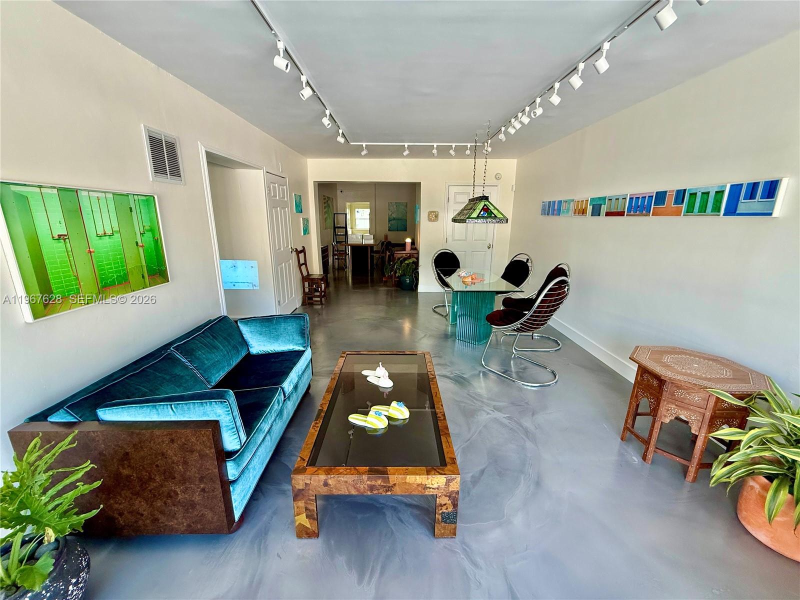 A living and dining area features a teal velvet sofa, glass tables, and gray flooring — 7613 Biscayne Blvd, Miami FL 33138, MIAMI, FL