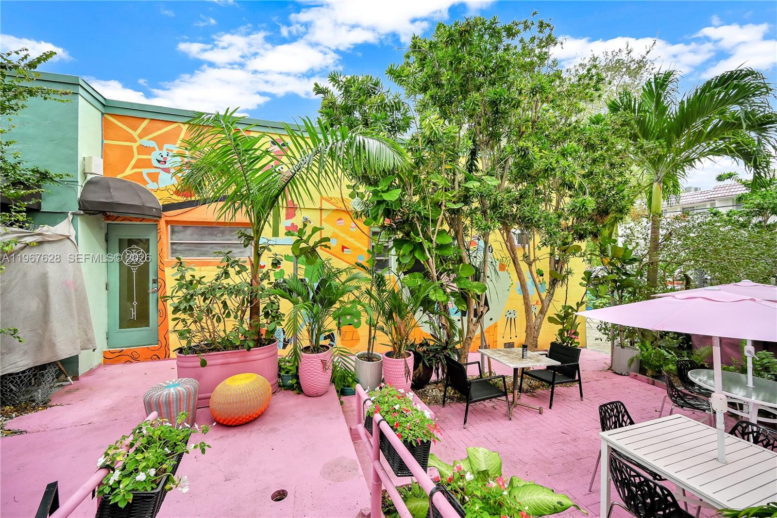 An outdoor patio features a pink painted floor, a colorful mural, and various potted plants — 7613 Biscayne Blvd, Miami FL 33138, MIAMI, FL