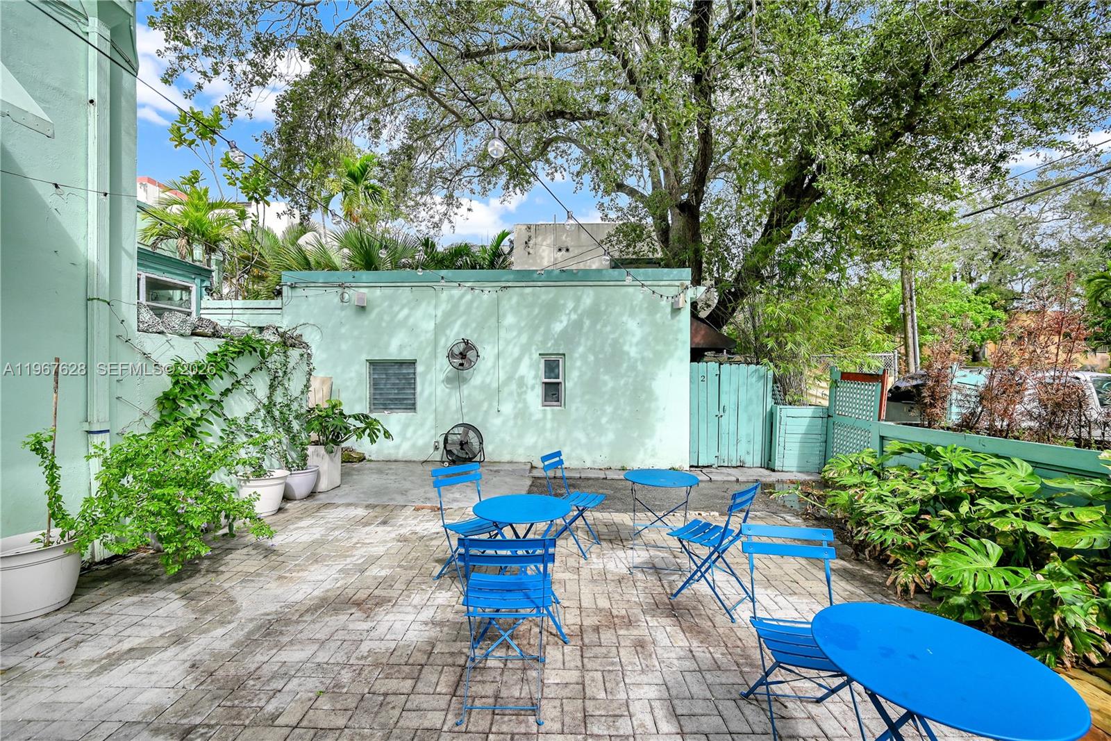 An outdoor patio features blue metal furniture on a paved surface against a green building — 7613 Biscayne Blvd, Miami FL 33138, MIAMI, FL