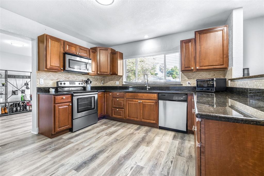 A kitchen features wood cabinets, stainless steel appliances, dark granite countertops, and light wood flooring — 4116 N MARGUERITE STREET, TAMPA, FL