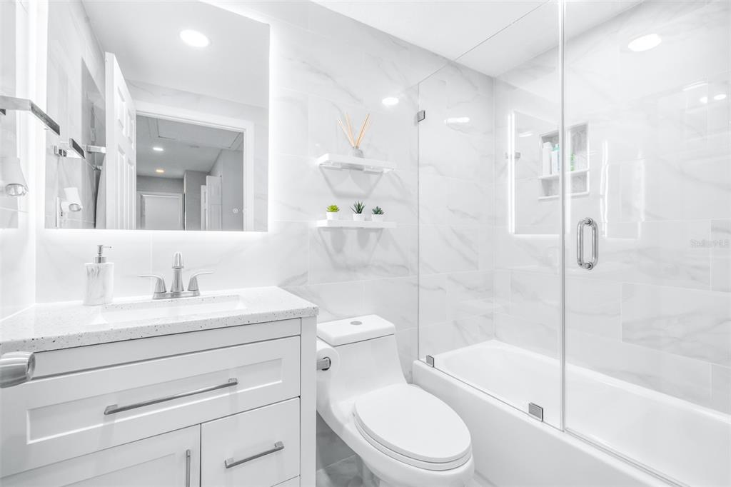 A bright, modern bathroom features a white vanity, a toilet, and a glass-enclosed shower — 4116 N MARGUERITE STREET, TAMPA, FL
