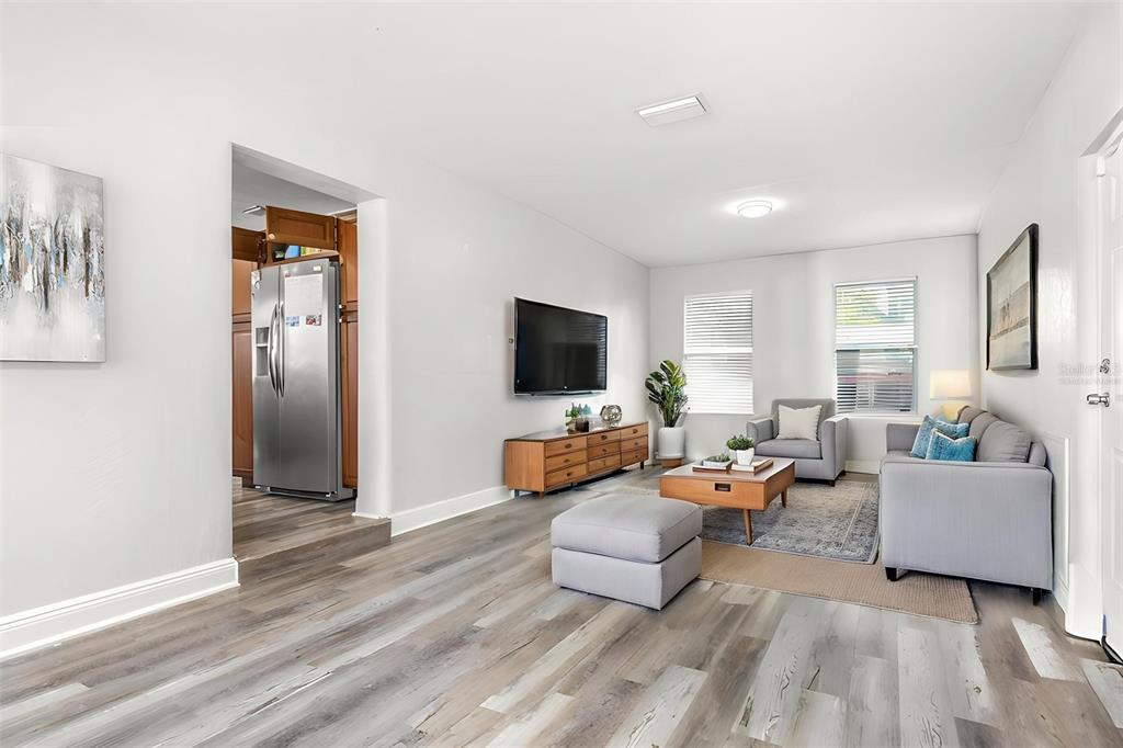 A living room features light wood-look flooring, a gray sofa, and a wall-mounted television — 4116 N MARGUERITE STREET, TAMPA, FL