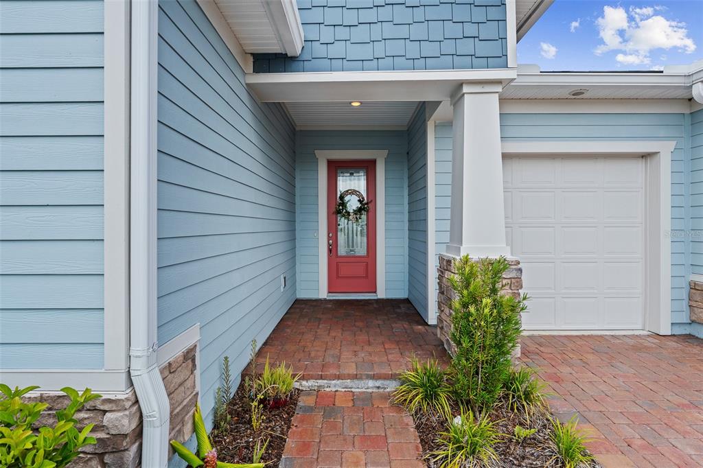 A blue house exterior features a red front door, stone accents, and a brick walkway — 83 REVERIE DRIVE N, PALM COAST, FL