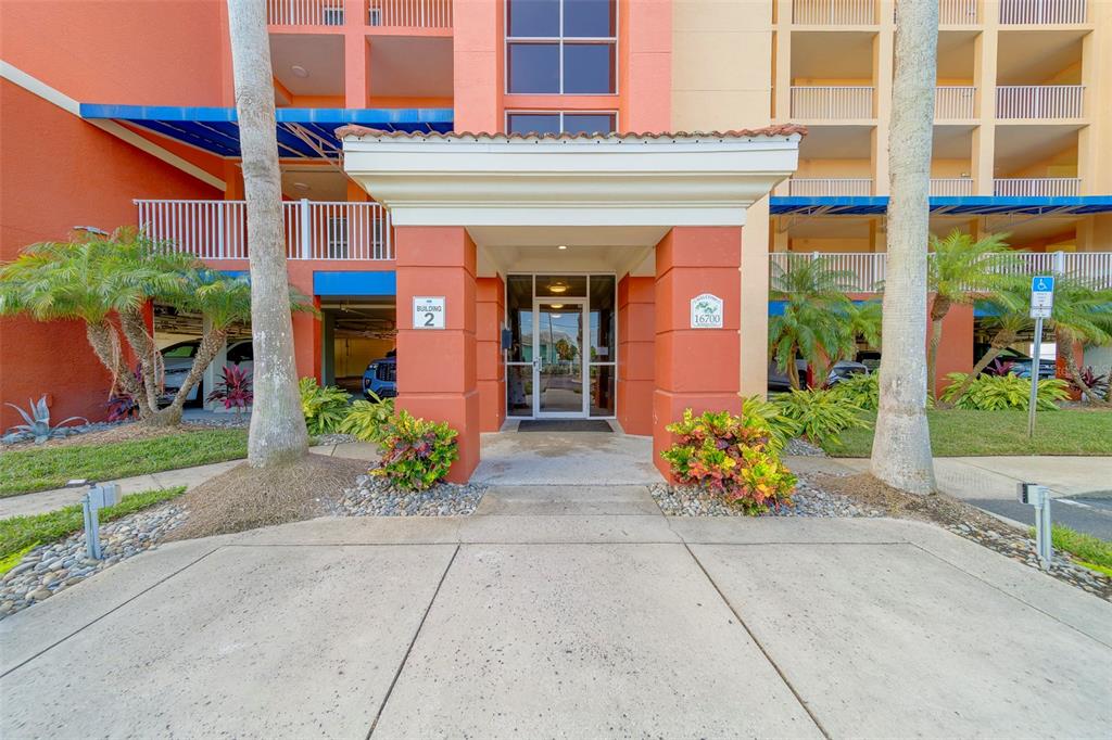 The exterior entrance of a multi-story apartment building features a covered walkway and palm trees — 16700 GULF BOULEVARD UNIT 423, NORTH REDINGTON BEACH, FL