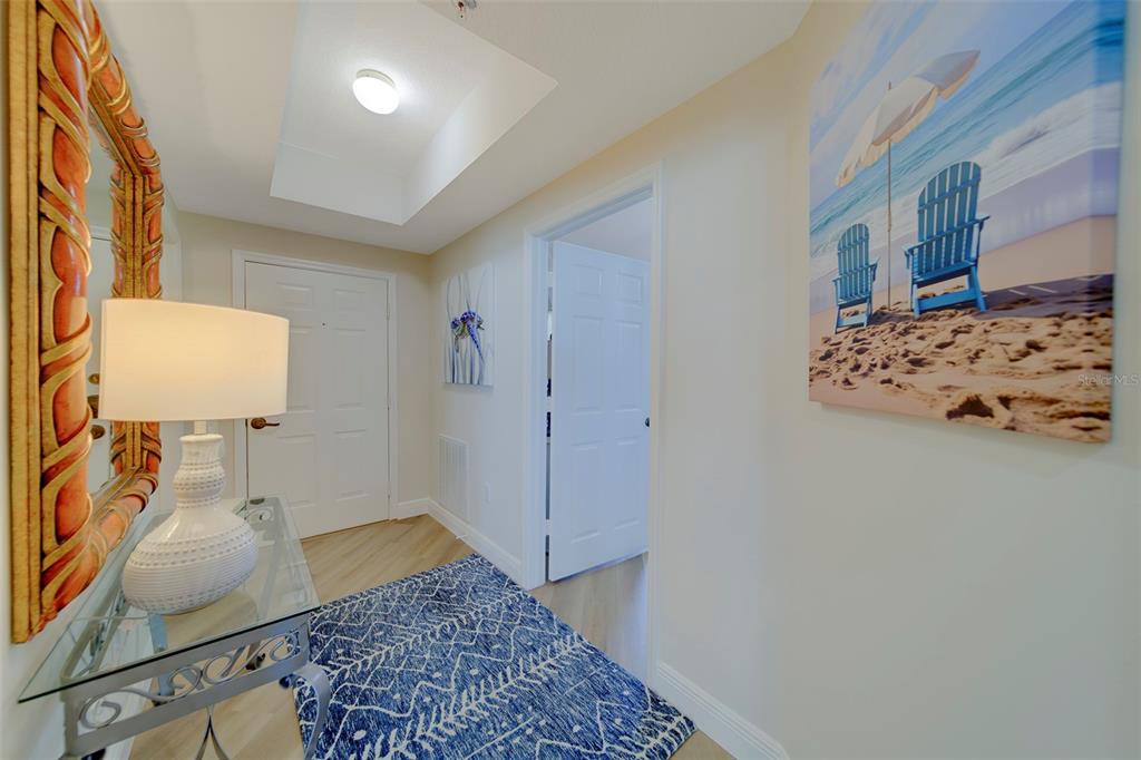 A hallway features a glass console table, a patterned blue rug, and beach-themed wall art — 16700 GULF BOULEVARD UNIT 423, NORTH REDINGTON BEACH, FL